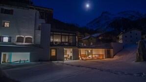 A modern building with large glass windows, a balcony, and a snow-covered landscape with mountains in the background.