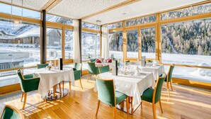 A restaurant with tables set for dining, large windows with a snowy mountain view, and wooden flooring.