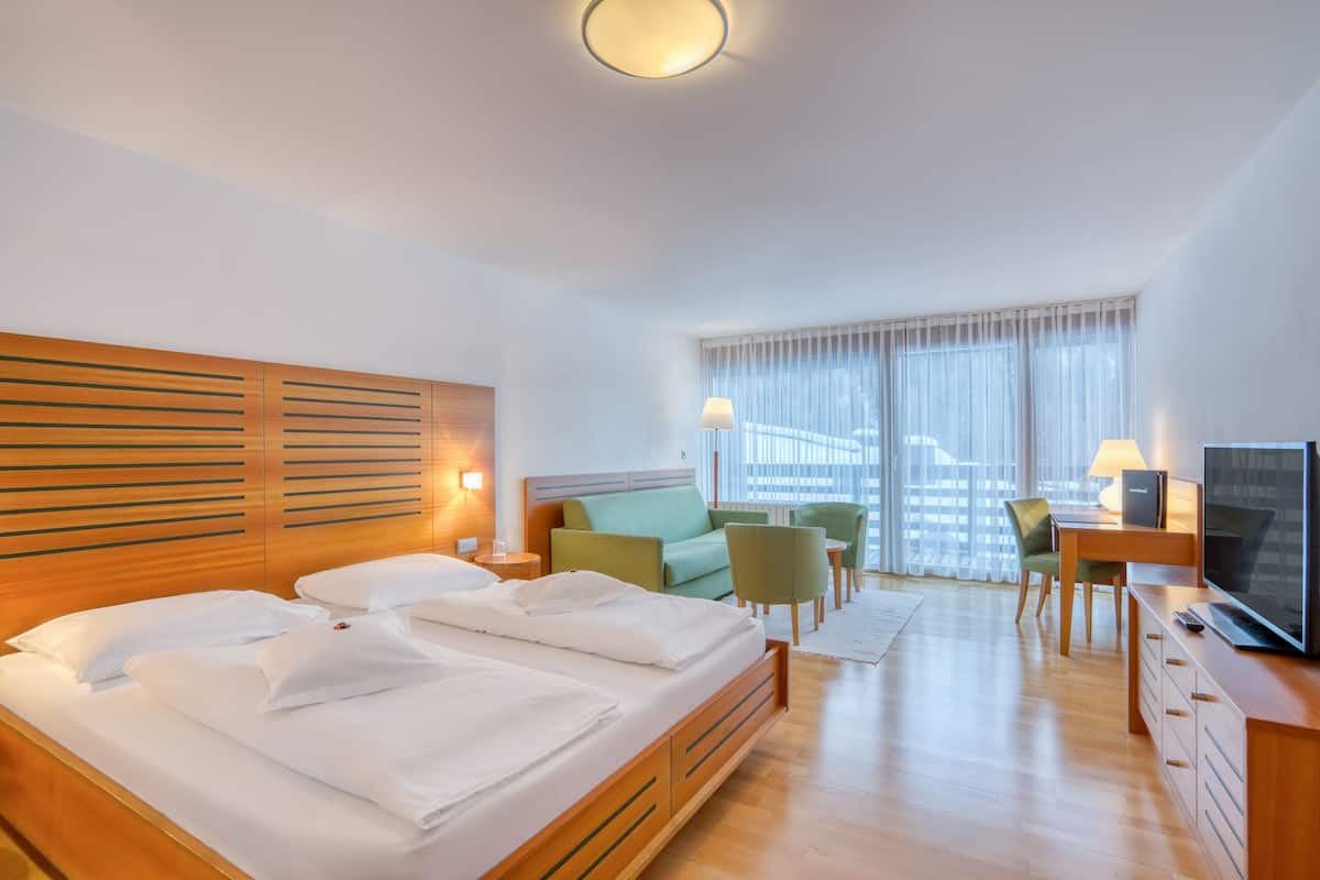Una habitación de hotel moderna con una cama grande, un escritorio con televisor y una zona de estar con sillas.