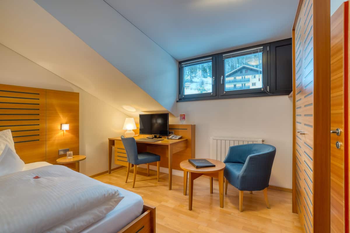 Una habitación de hotel moderna con cama, escritorio, ordenador y dos sillas.