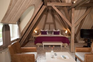 Ein gemütliches, dreieckiges Schlafzimmer mit einem großen Bett, zwei Nachttischen, einem Flachbildfernseher und einem kleinen Tisch mit einer Flasche und Gläsern.