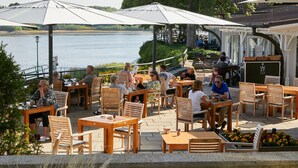 Ulkoterassi, jossa on puupöytiä ja -tuoleja, aurinkovarjoja ja näkymä järvelle.
