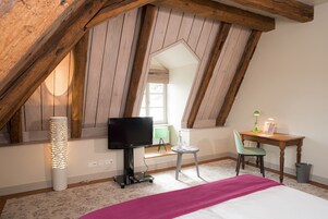 Un dormitorio con techo inclinado, una cama, un escritorio con silla, un televisor y una lámpara.