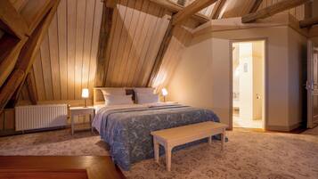 Ein Schlafzimmer mit schrägen Wänden, einem Bett mit floralem Überwurf, einem Nachttisch mit Lampen, einer Bank und einem Heizkörper.