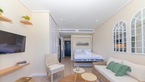 A compact hotel room with a bed, a sofa, a chair, a TV, and a small table. - 16 on Bree 1218 (Cape Town)