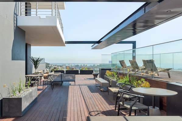 Une terrasse sur le toit, aménagée avec des espaces de détente en plein air, des jardinières et offrant une vue sur la ville.