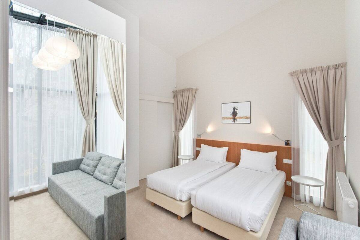 A hotel room with a sofa, two single beds, a small table, and a picture on the wall.