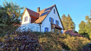 Een huis met twee verdiepingen, een schuin dak, zonnepanelen en een tuinkamer.