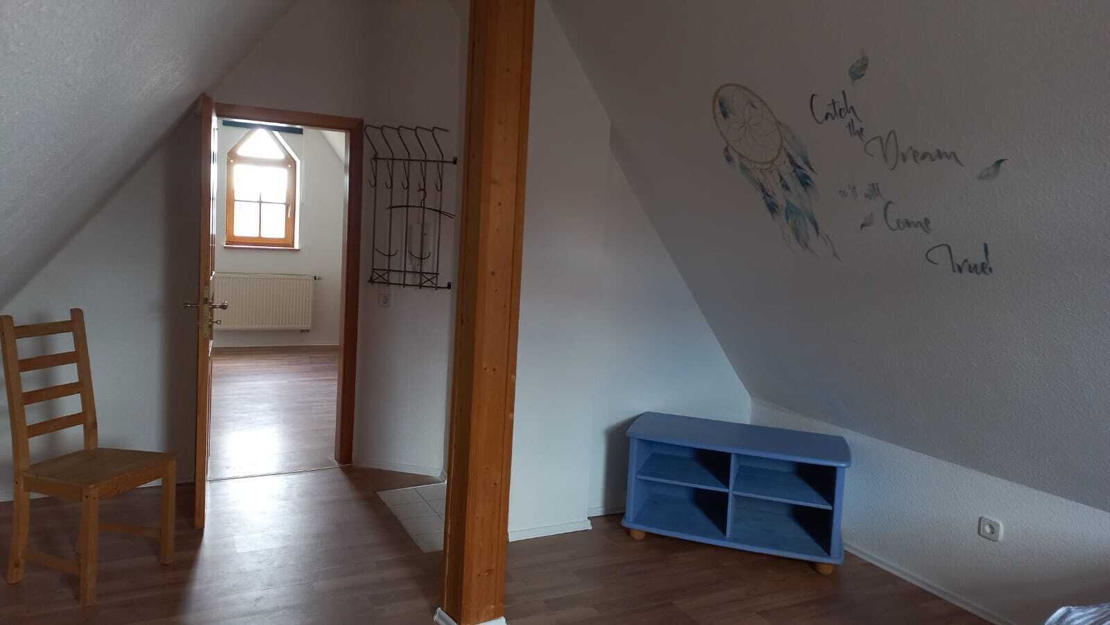 Una habitación con techo inclinado, una silla de madera, un mueble azul para almacenamiento y una pared con mensajes inspiradores.
