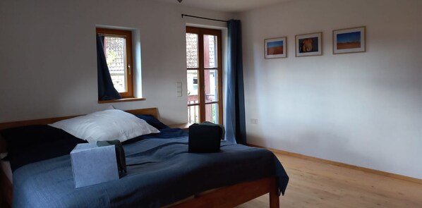 Een slaapkamer met een bed, twee ramen, een deur en drie ingelijste foto's aan de muur.
