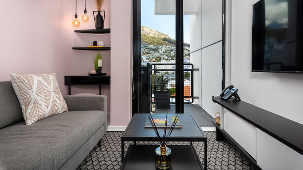 A modern living room with a grey sofa, black coffee table, and a view of a cityscape through a glass door. - The Flamingo 708 (Cape Town)