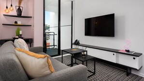 A modern living room with a grey sofa, black coffee table, and a mounted TV. There are black shelves with decorative items and a glass door leading outside. - The Flamingo 708 (Cape Town)