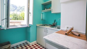 Une cuisine aux murs de couleur turquoise, avec un carrelage à motifs et une fenêtre donnant sur un paysage verdoyant.
