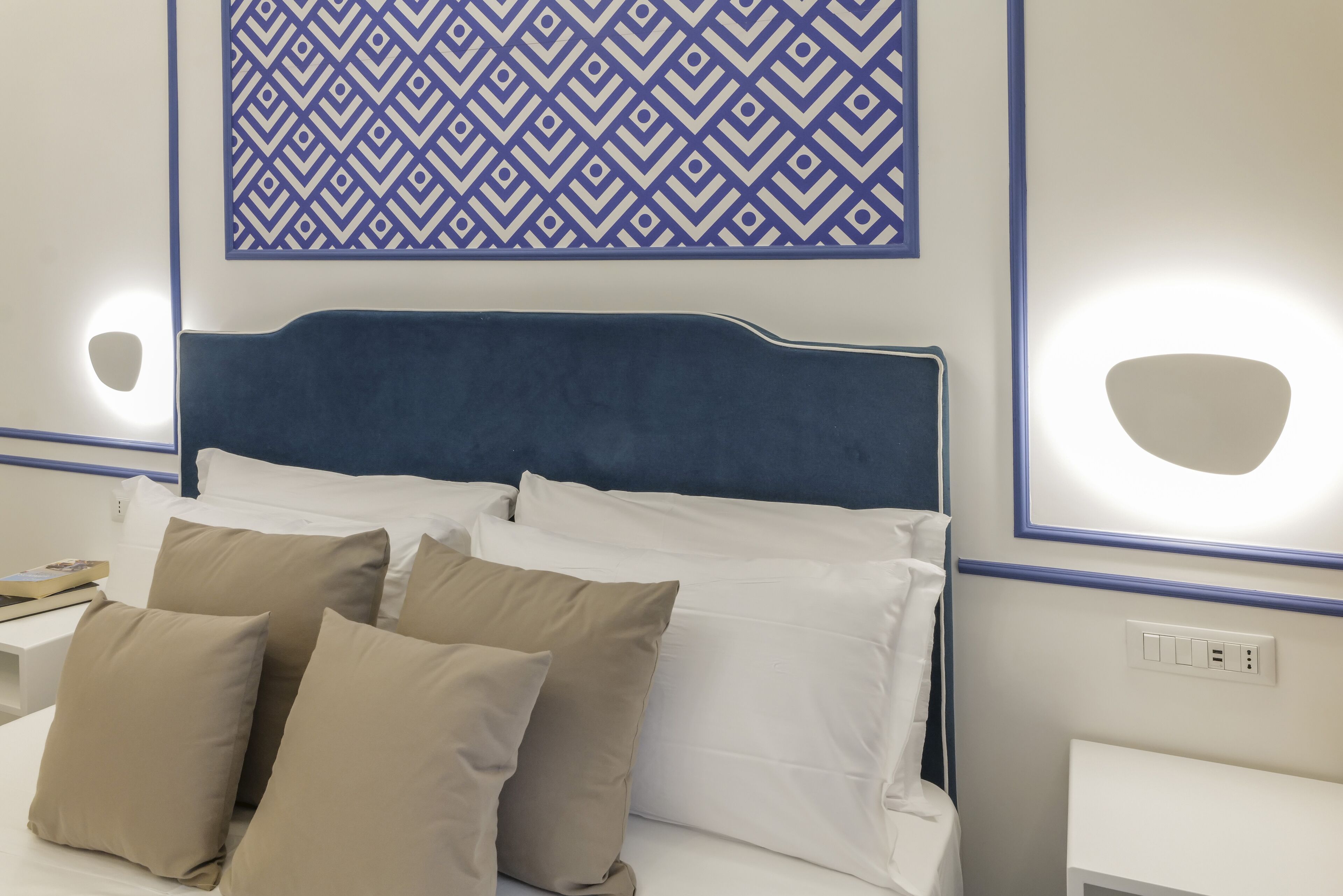 Ein Hotelzimmer mit einem Bett, beigen Kissen, einem blauen Kopfteil und einer Wanddekoration mit Muster.