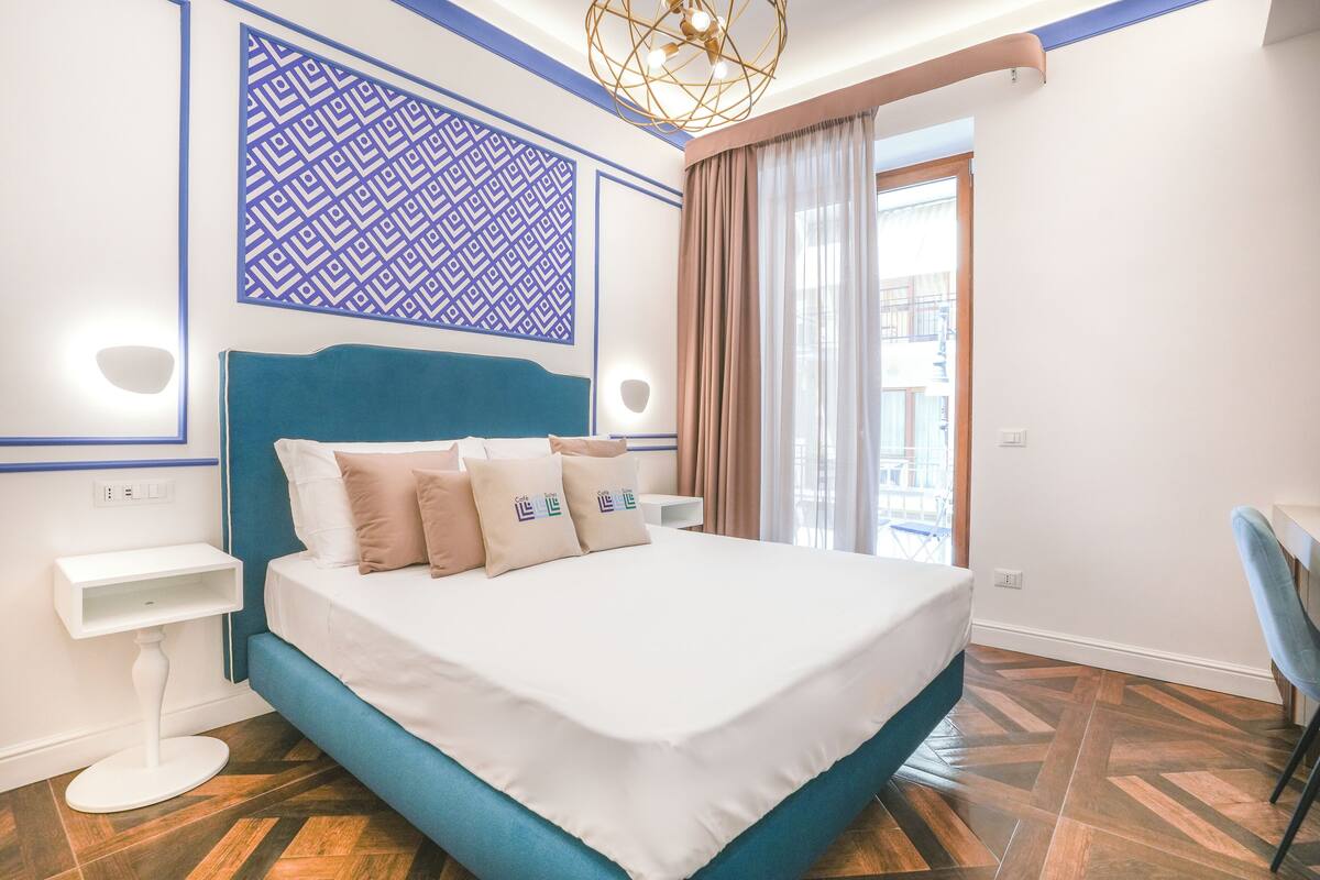 Une chambre d’hôtel moderne avec un grand lit, un panneau décoratif au mur, une table de chevet et une vue sur l’extérieur.