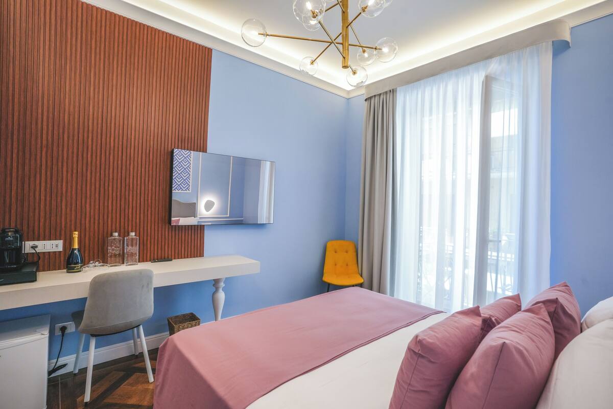 Une chambre d’hôtel avec un lit, un bureau et une chaise, une télévision et une fenêtre avec des rideaux.
