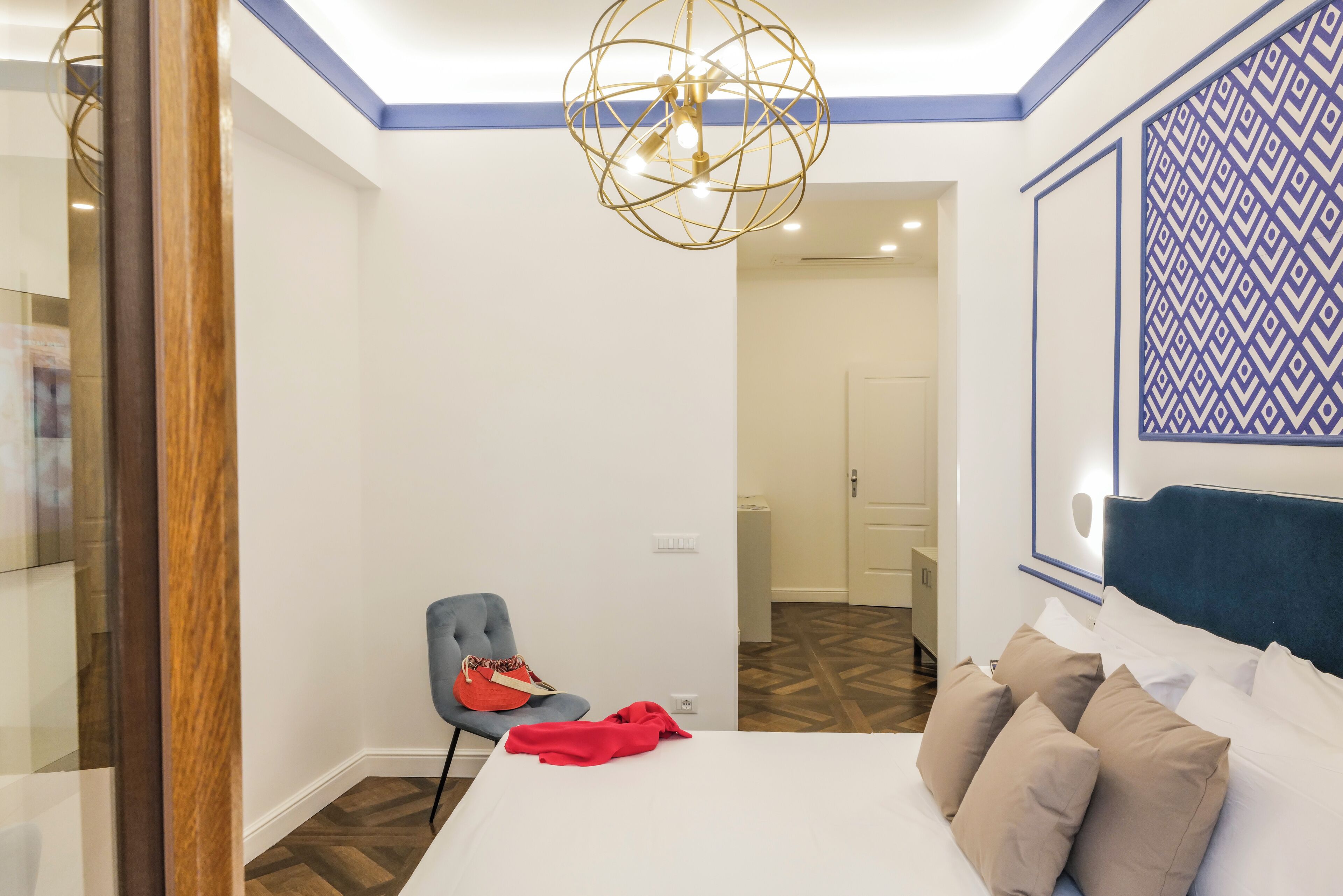 A bedroom with a bed, a chair, a red blanket, and a decorative wall piece.