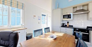 A modern kitchen with a wooden dining table, chairs, and a microwave. - Stunning Beach House - Sleeping 4 in 2 Bedrooms - Pool and Beach Access Included. (Filey)