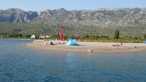 A beach with tents and people sunbathing, a red communication tower, and mountains in the background.