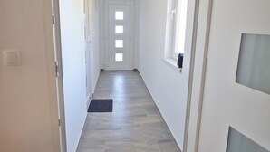 A narrow hallway with a tiled floor, white walls, and a door at the end.