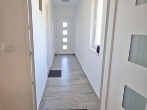 Um corredor estreito com chão de azulejos, paredes brancas e uma porta no final.