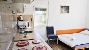 A compact hotel room with a kitchenette, a bed, and a chair.