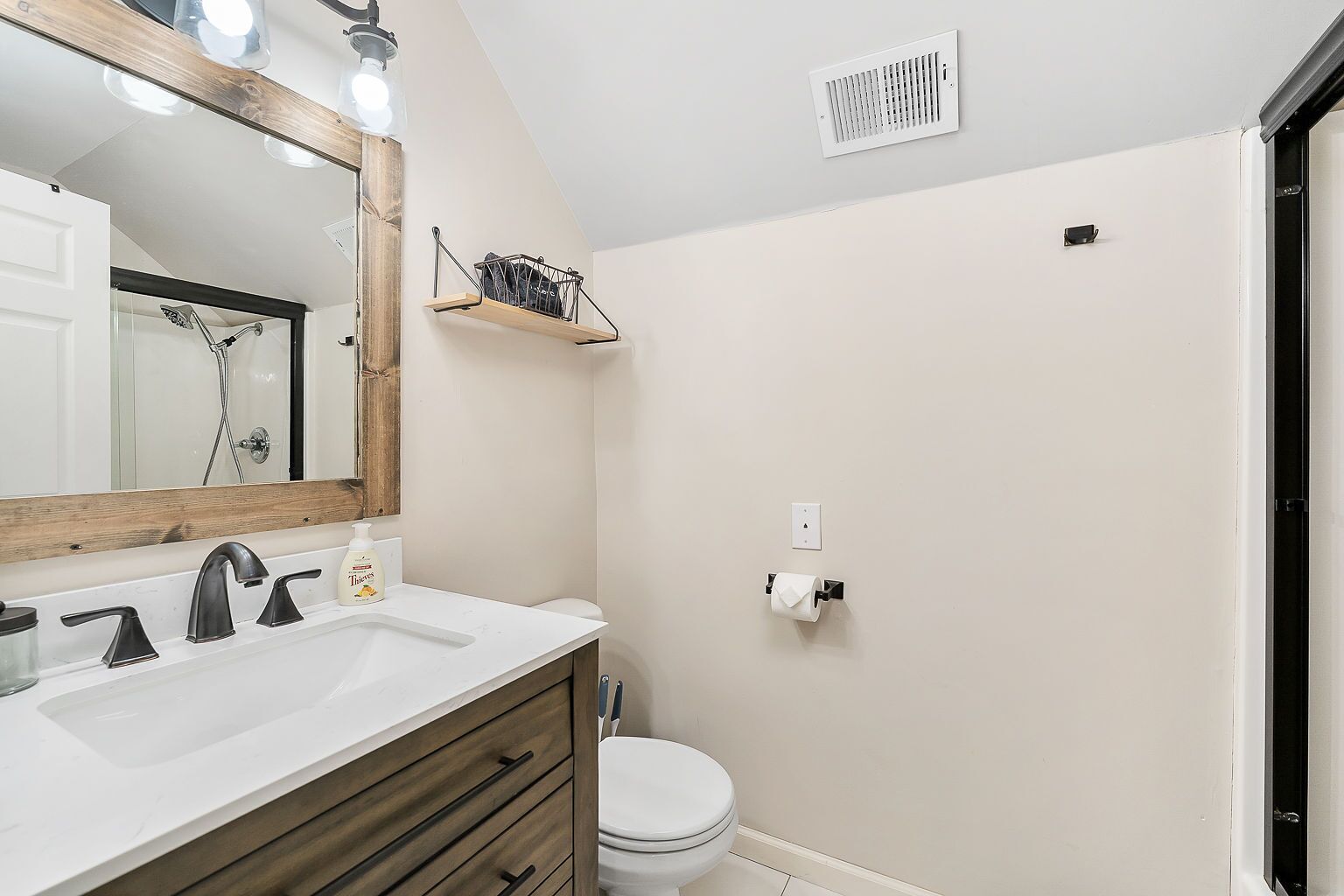 Un baño con tocador de madera, espejo, ducha e inodoro.
