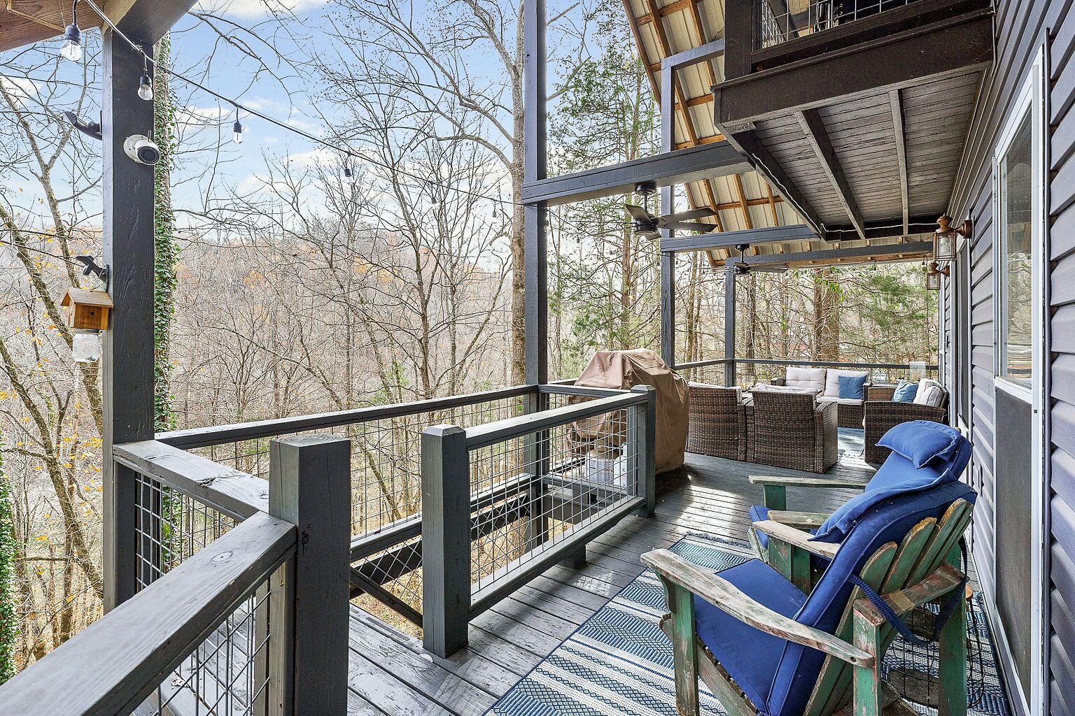 A covered outdoor deck with wicker furniture and a view of trees.