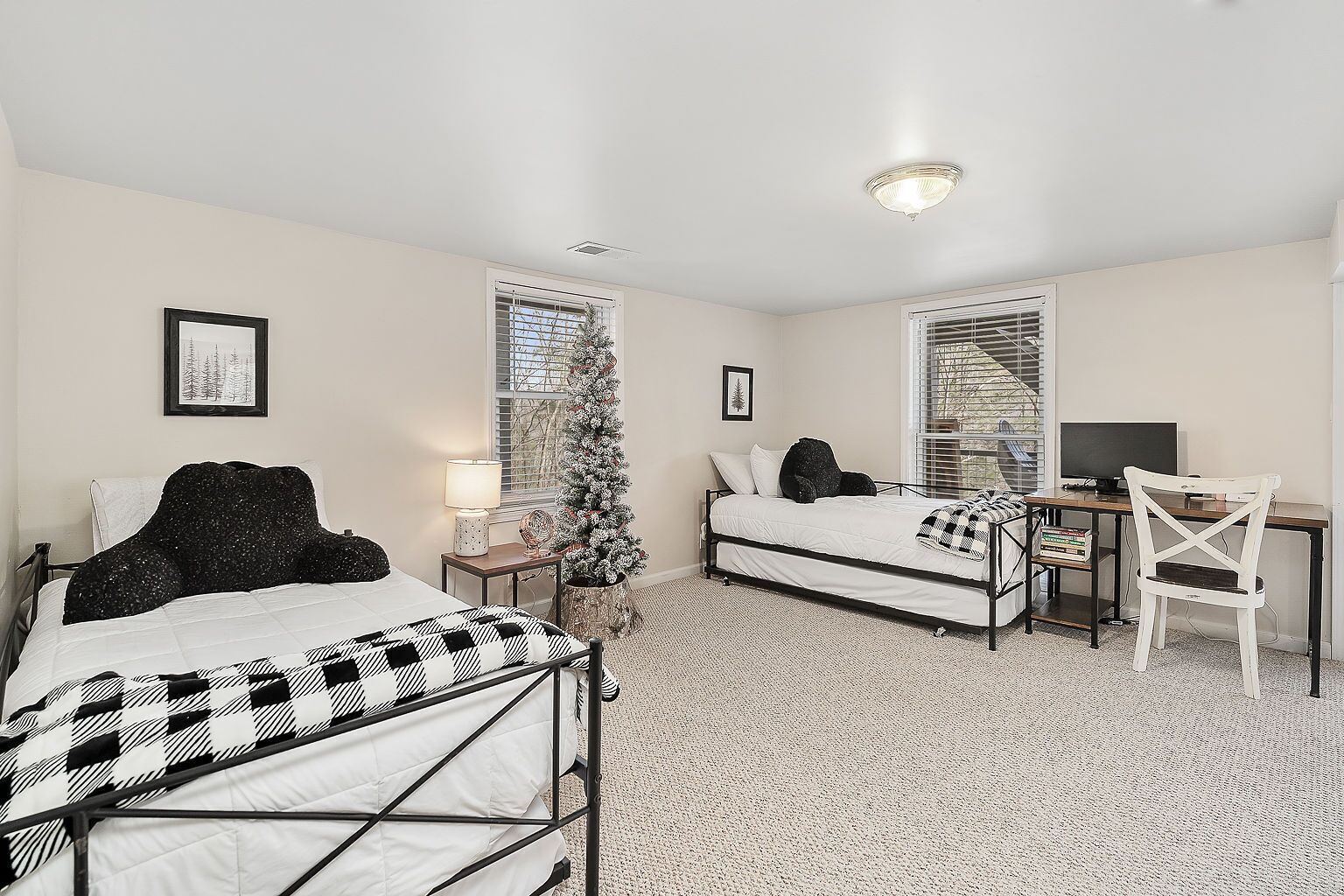 A bedroom with two beds, a desk, a chair, a Christmas tree, and a window with blinds.