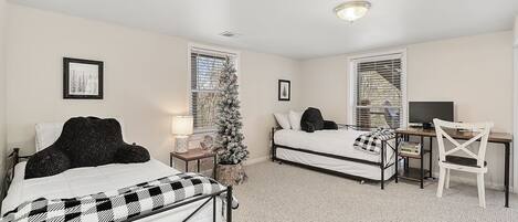 A bedroom with two beds, a desk, a chair, a Christmas tree, and a window with blinds.