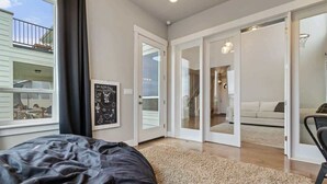 Une chambre à coucher avec un lit, un tableau noir avec des inscriptions, une porte donnant sur un balcon, et une vue sur un balcon doté d’une balustrade.