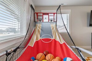 A basketball court with a red floor, two basketball hoops, and a netted enclosure.