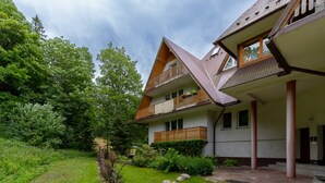 A two-story house with a sloped roof, wooden balconies, and a garden area with rocks and greenery. - Stylish Apartment with Balcony | Close to Mountain Trails (Zakopane)