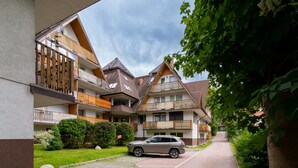 A residential building with multiple balconies, a paved driveway, and a parked SUV. - Stylish Apartment with Balcony | Close to Mountain Trails (Zakopane)