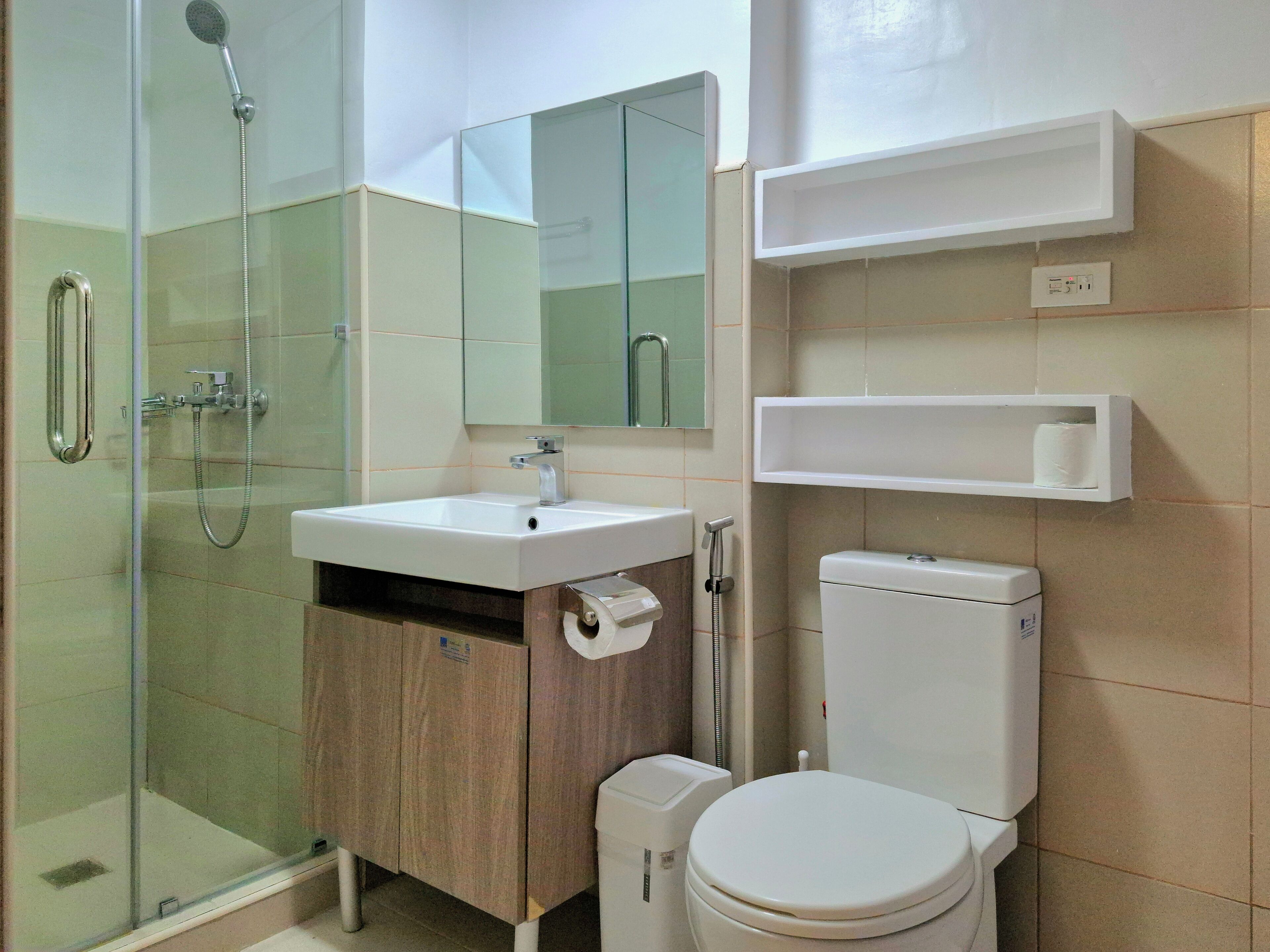 A bathroom with a glass shower enclosure, a sink with a mirror above it, a toilet, and two white shelves.