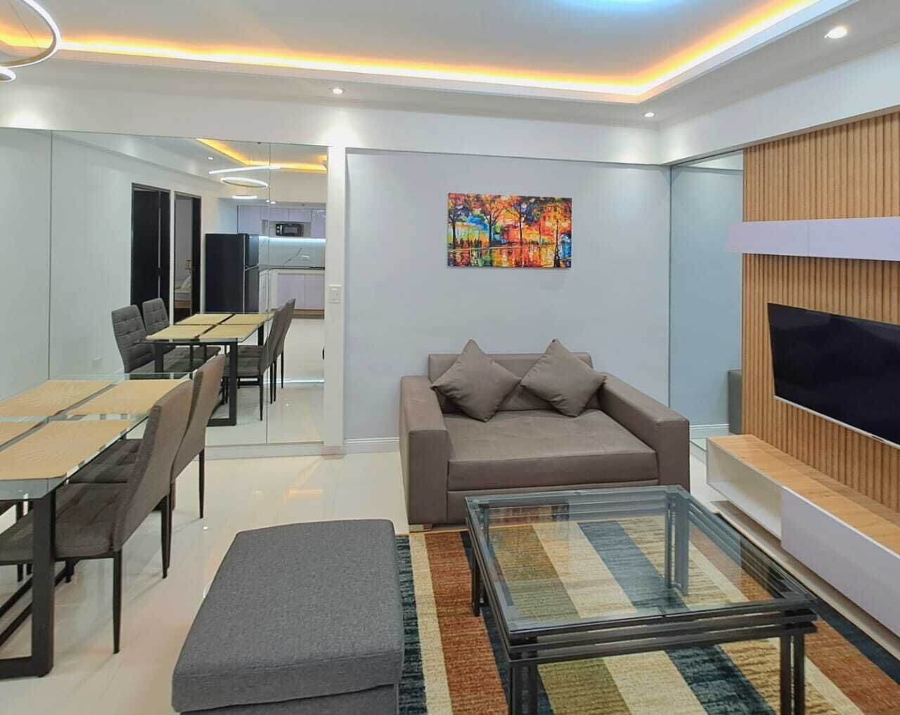 A modern living room with a sofa, a coffee table, and a TV. There is a dining area with chairs and a table.