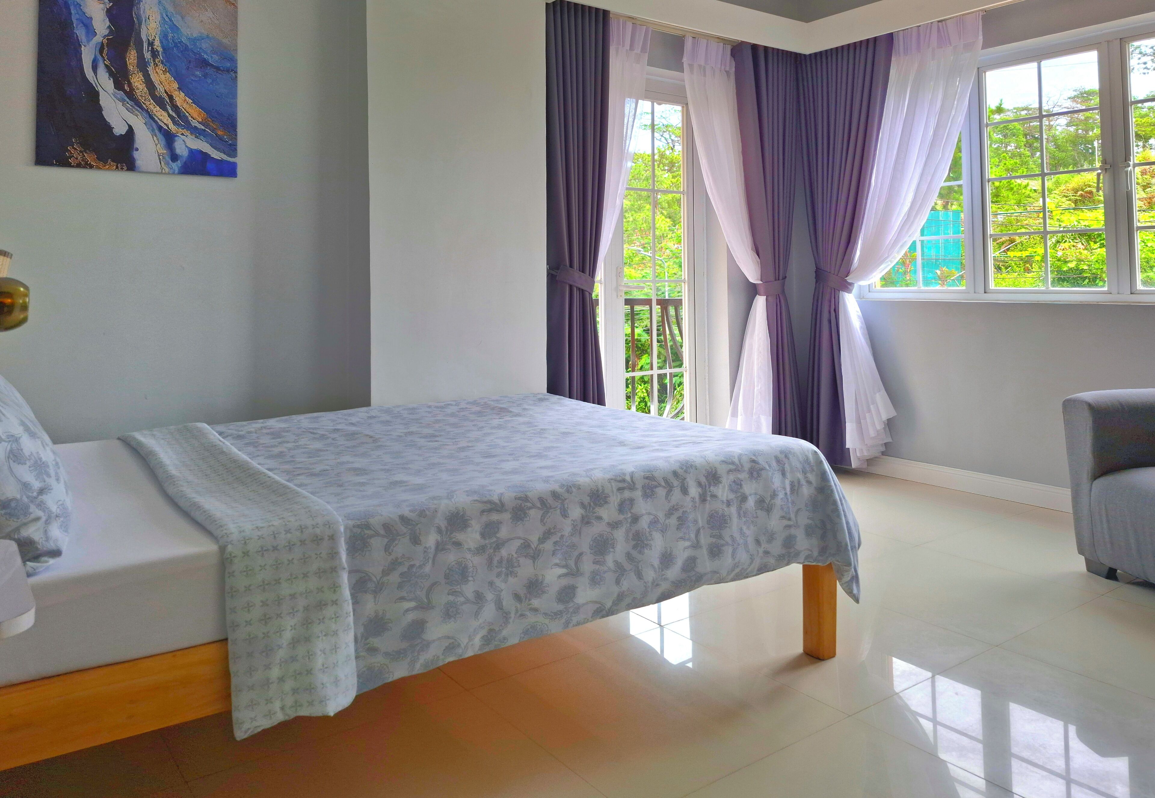 Un dormitorio con una cama, una ventana con cortinas, una silla y un cuadro en la pared.