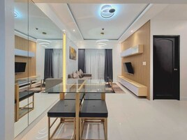 A modern living room with a glass dining table, sofas, and a TV mounted on the wall.