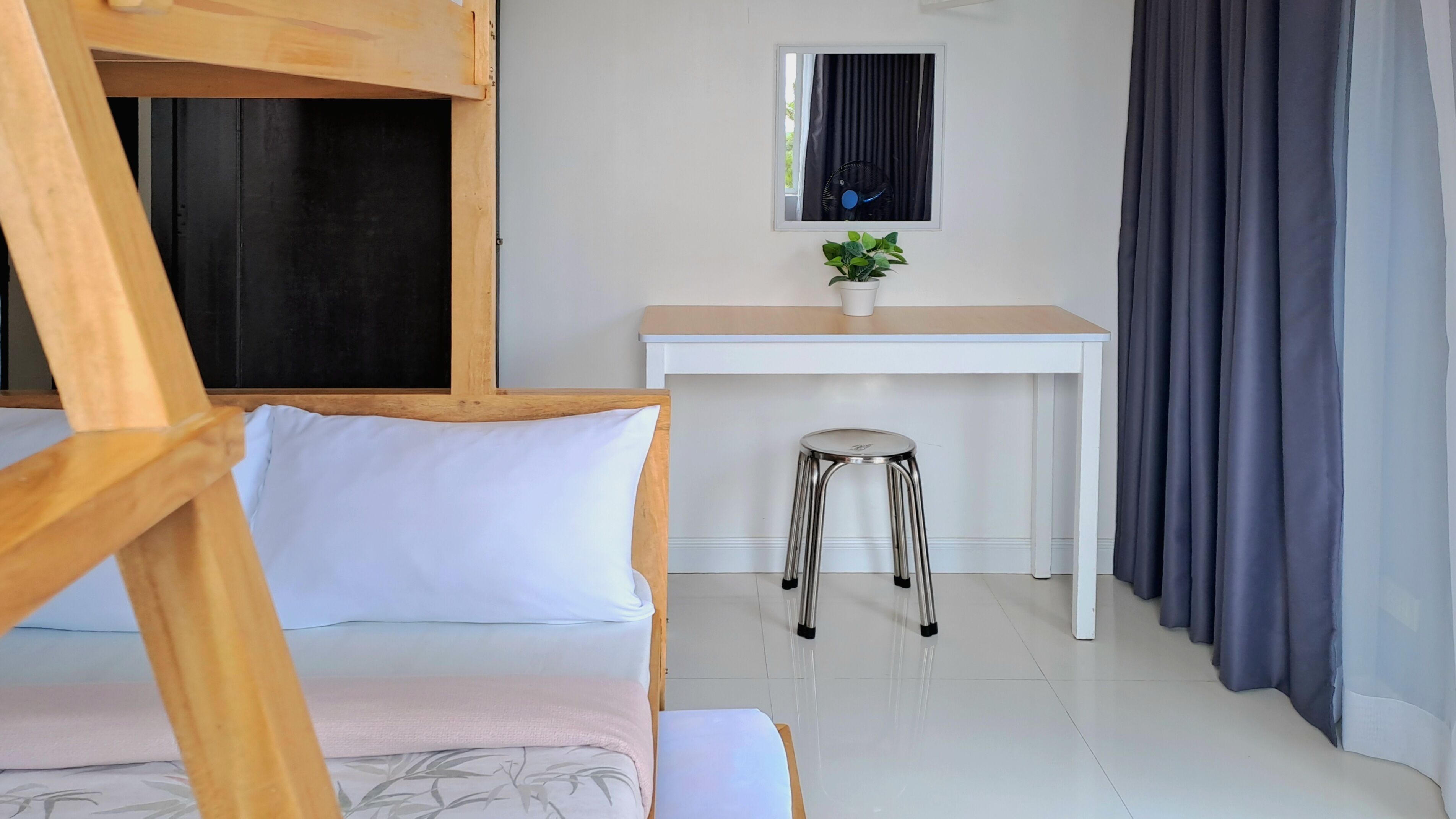 A room with a bunk bed, a desk, a chair, and a potted plant.