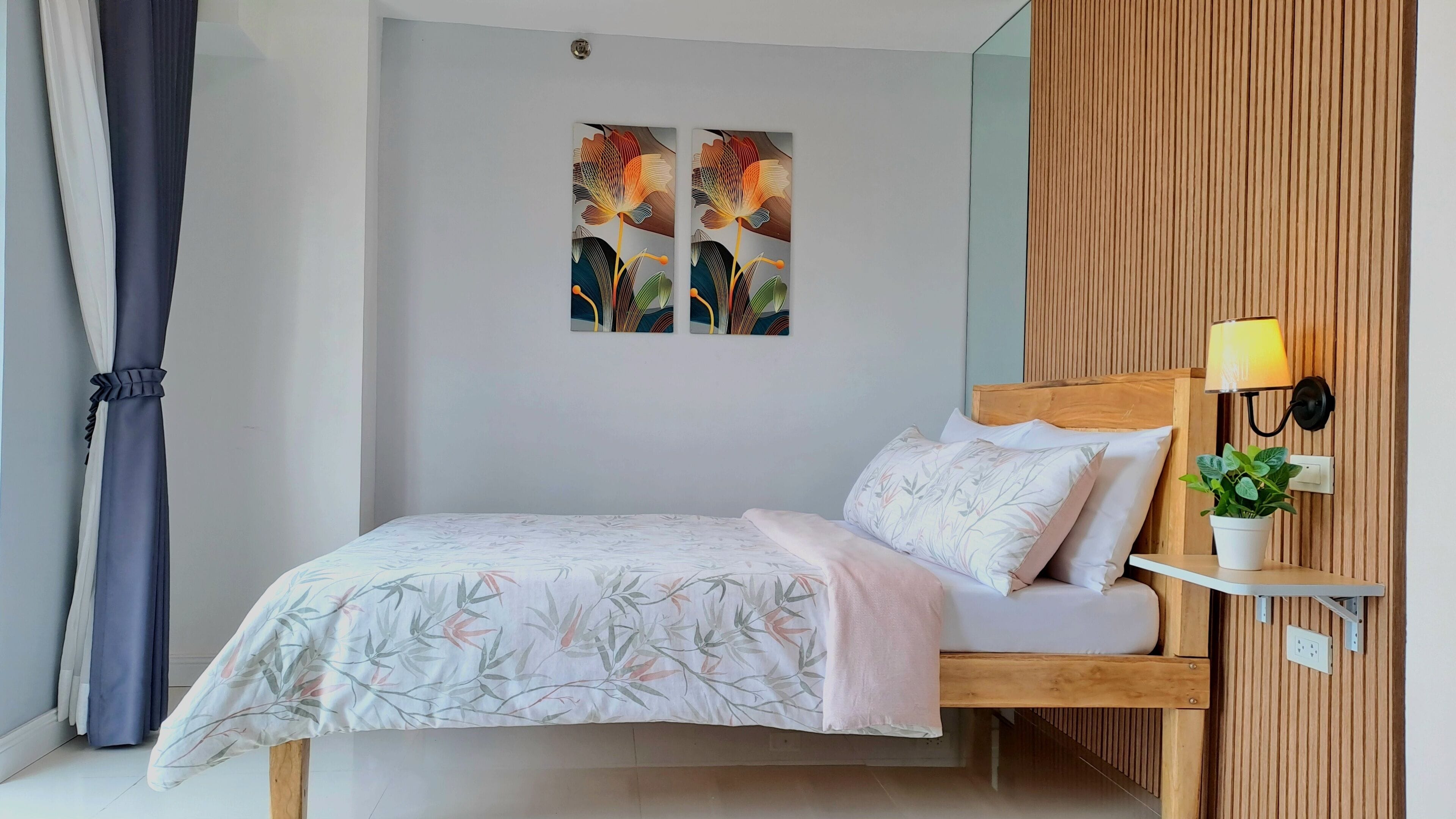 Une chambre à coucher comprenant un lit, une table de chevet avec une lampe, une étagère murale avec une plante et deux œuvres d’art accrochées au mur.