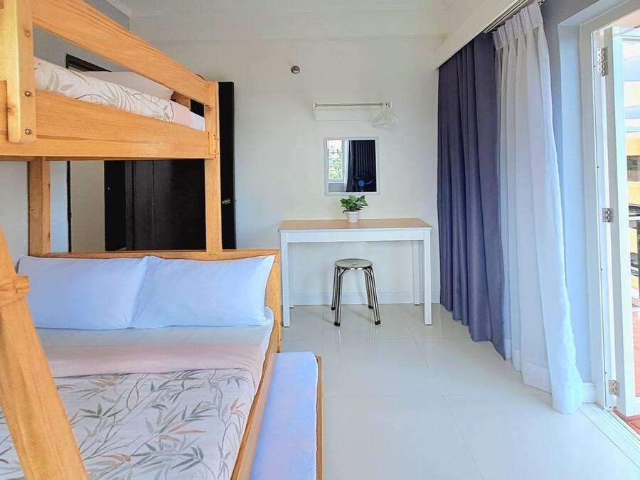 Una litera con escritorio y silla, una ventana pequeña y un panel corredizo hacia un área exterior.