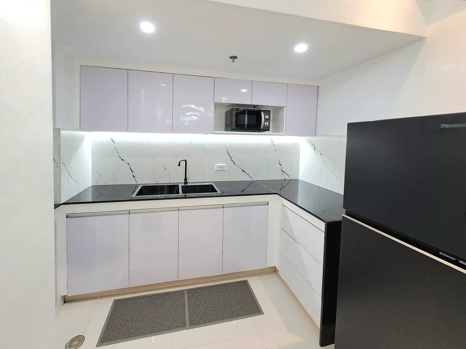 A compact kitchen with white cabinets, a black countertop, a built-in microwave, and a black refrigerator.