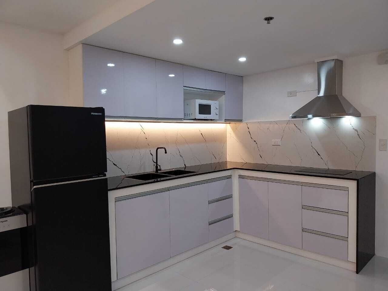 A modern kitchen with a black refrigerator, white cabinets, a stainless steel range hood, and a microwave on the countertop.