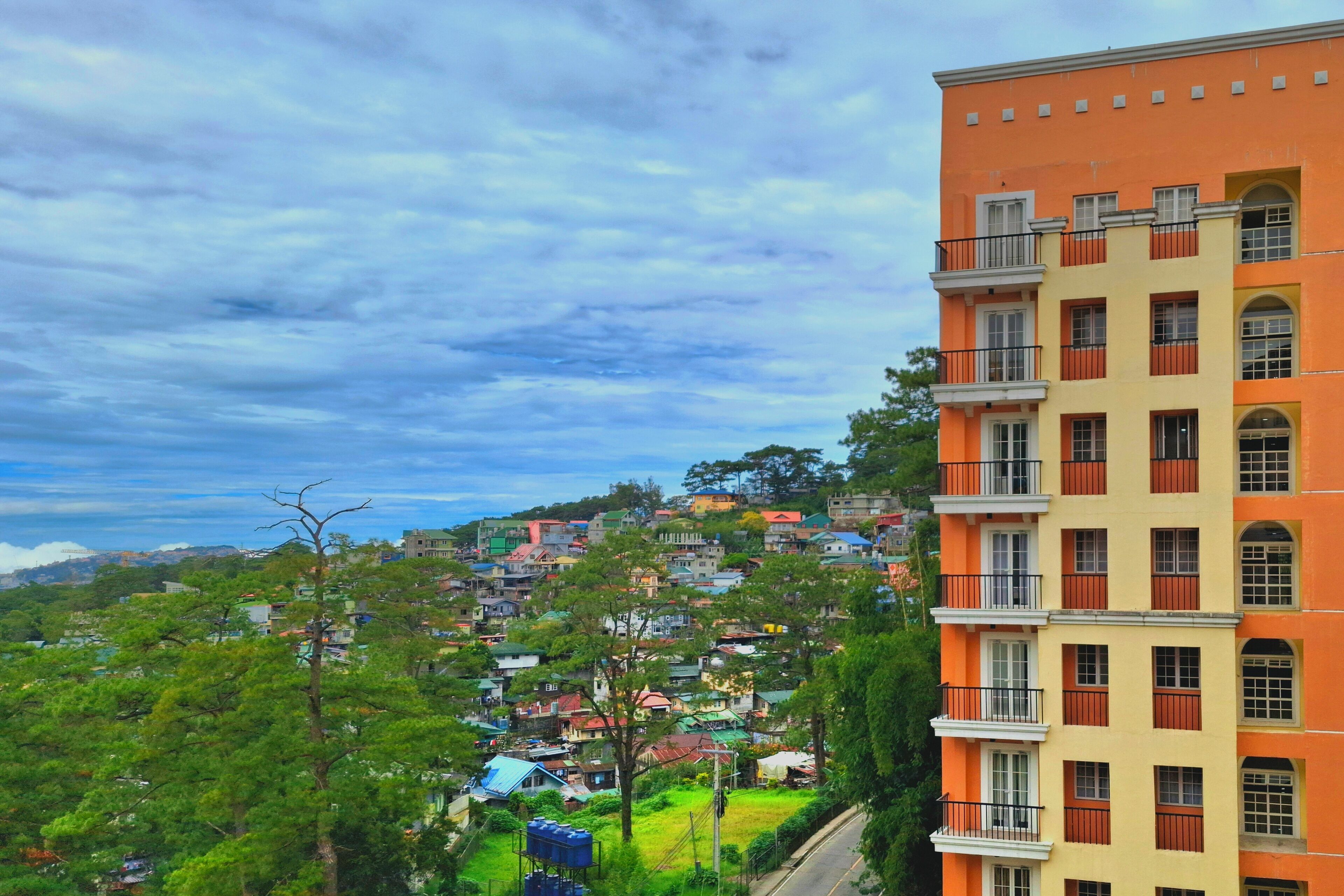A multi-story building with balconies and a view of a residential area with houses and greenery.