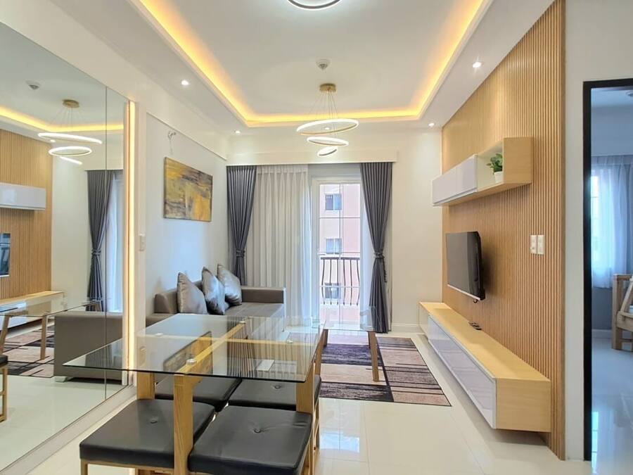 A modern living room with a glass coffee table, a sofa, and a TV mounted on the wall.