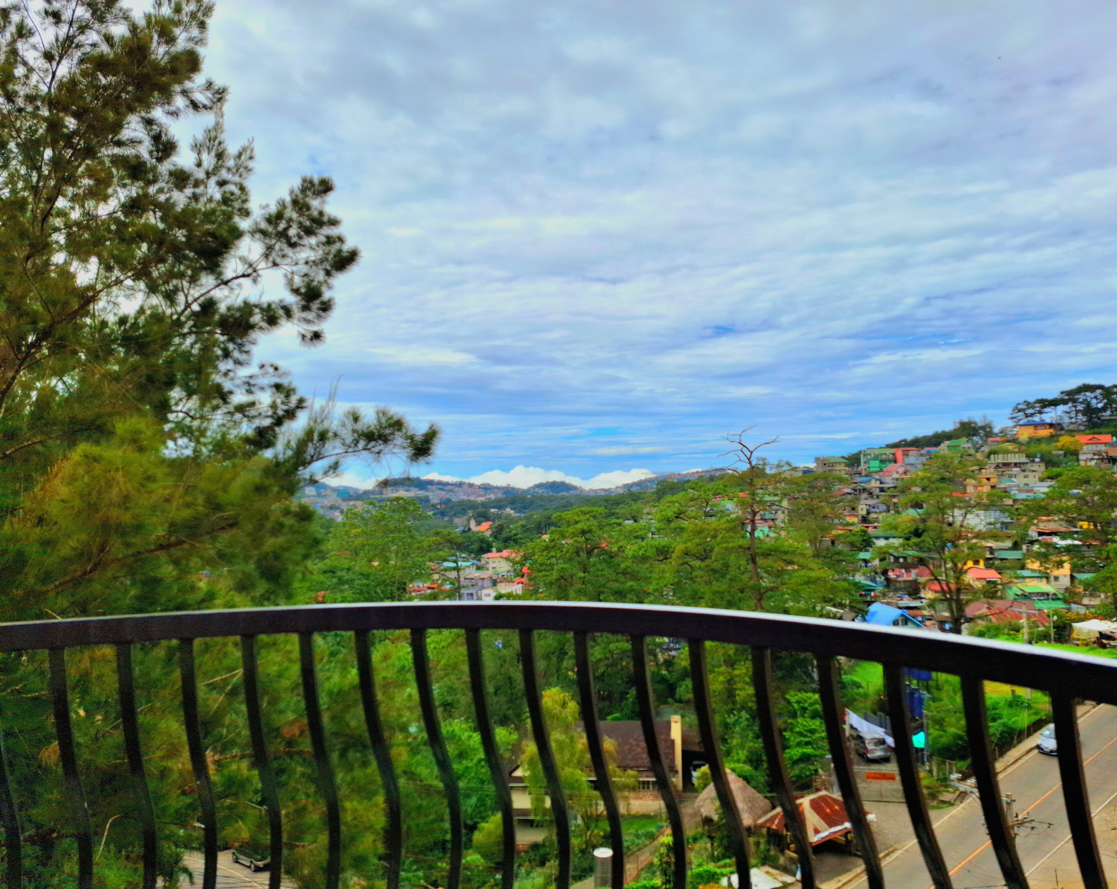 Un balcon donnant sur une ville perchée sur une colline, des arbres et une route.