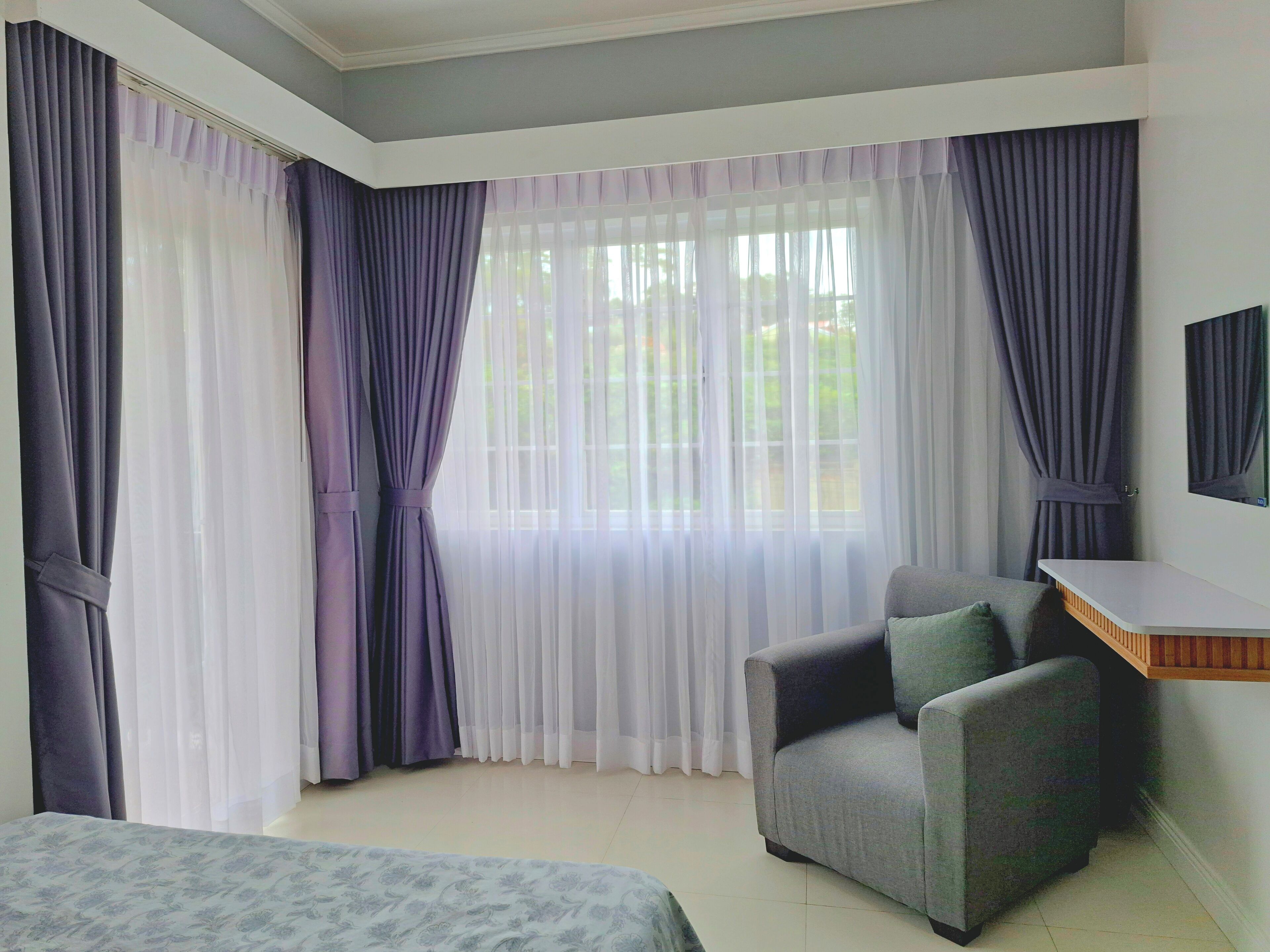 A bedroom with a bed, a chair, a desk, and a window with curtains.