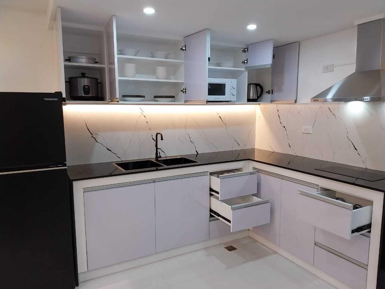 Une cuisine moderne avec des armoires blanches, un comptoir noir et des appareils électroménagers intégrés, notamment un réfrigérateur, un four à micro-ondes et une cuisinière.