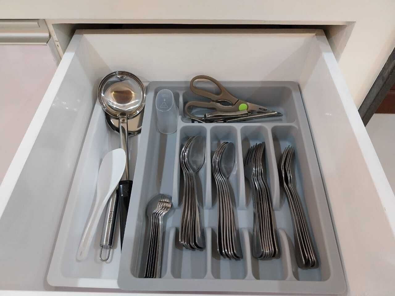 A drawer containing various utensils including forks, spoons, and a pair of scissors.