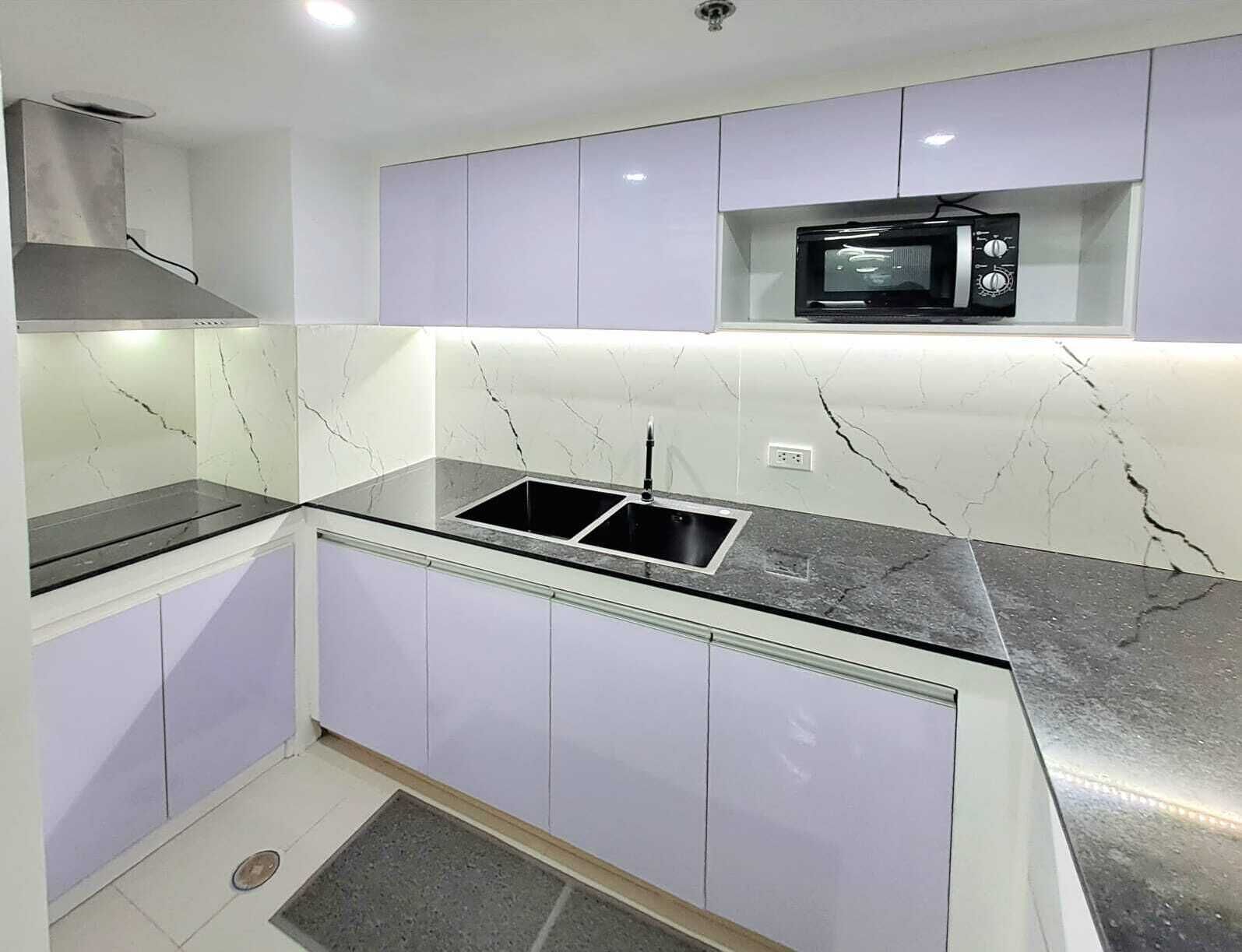 Una cucina con un piano di lavoro nero, un lavello in acciaio inossidabile e un forno a microonde sopra il bancone.